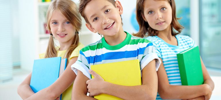 Portrait of happy classmates with books looking at camera in classroom