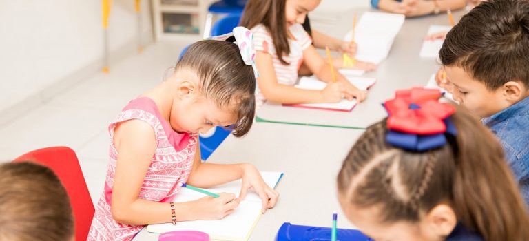Group of preschool kids working on a writing assigment in a classroom